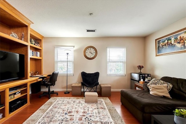 living area featuring visible vents, built in study area, a wealth of natural light, and wood finished floors
