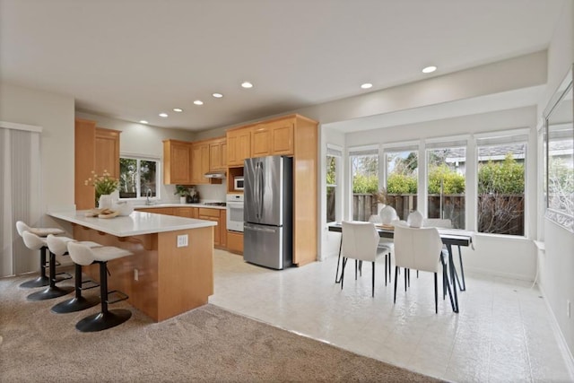 kitchen with sink, a breakfast bar area, stainless steel fridge, kitchen peninsula, and light brown cabinets