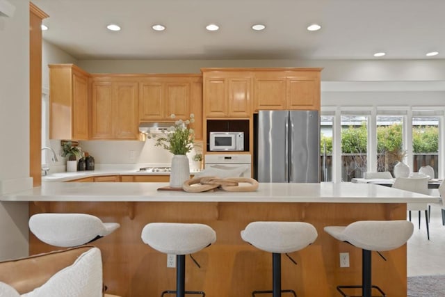 kitchen featuring white appliances, light brown cabinetry, kitchen peninsula, and sink