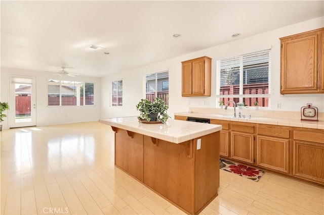 kitchen featuring sink, a kitchen breakfast bar, a center island, tile counters, and light wood-type flooring