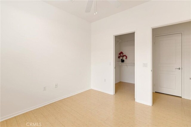 unfurnished bedroom featuring a closet, a walk in closet, ceiling fan, and light hardwood / wood-style flooring