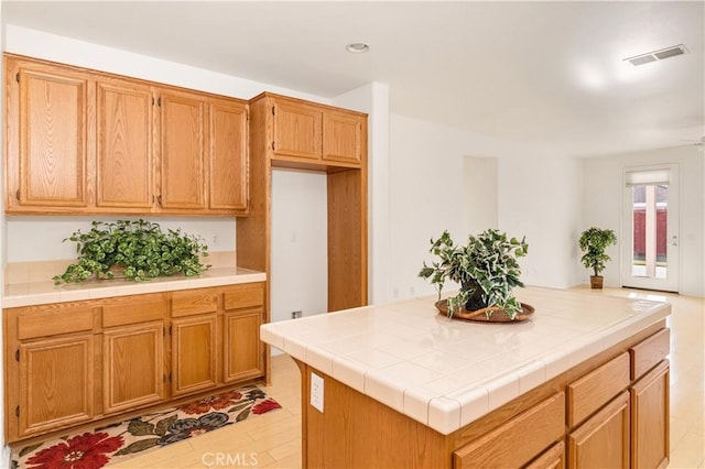 kitchen with tile countertops, a kitchen island, and light hardwood / wood-style flooring