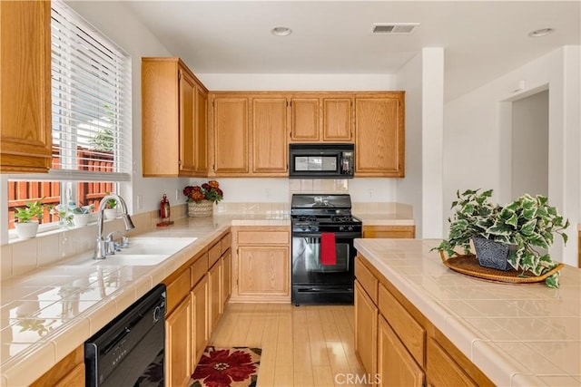 kitchen featuring light hardwood / wood-style flooring, sink, tile countertops, and black appliances