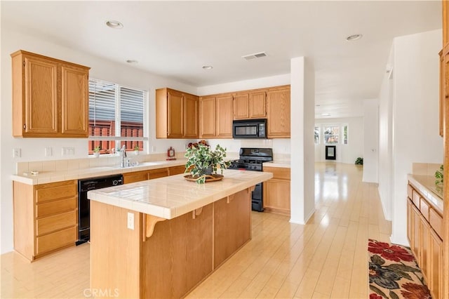 kitchen featuring a breakfast bar, a center island, tile counters, light hardwood / wood-style floors, and black appliances