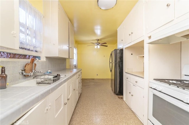 kitchen featuring gas range gas stove, black fridge, tile countertops, white cabinets, and backsplash