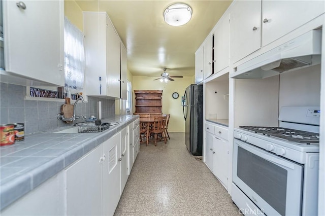 kitchen featuring white cabinetry, tile counters, white gas range oven, and black fridge