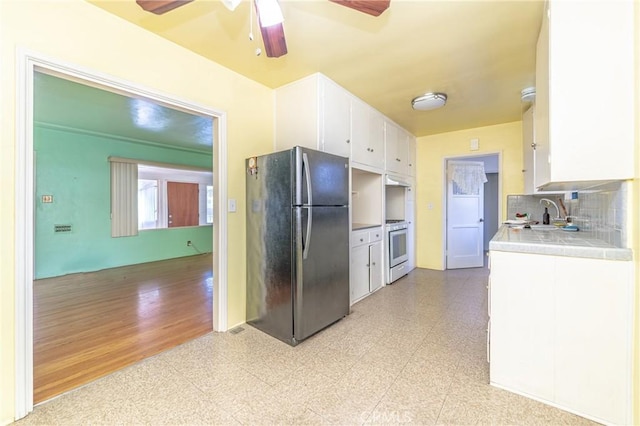 kitchen featuring white cabinetry, backsplash, white gas stove, and black fridge