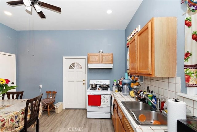 kitchen featuring sink, light hardwood / wood-style flooring, backsplash, tile counters, and white gas stove