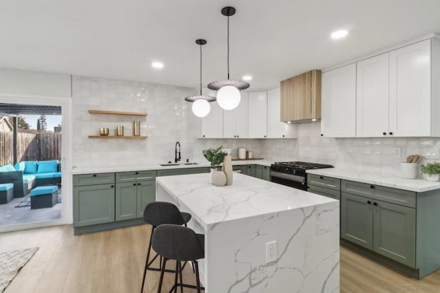 kitchen with sink, light stone counters, light wood-type flooring, black gas stove, and white cabinets