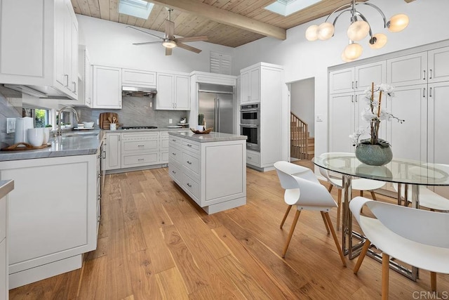 kitchen with sink, white cabinetry, a skylight, stainless steel appliances, and a kitchen island