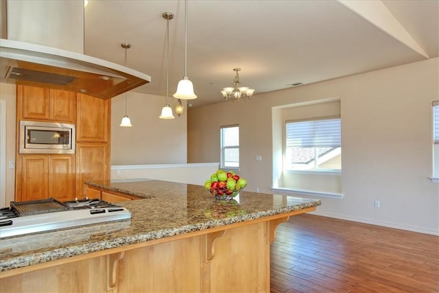 kitchen with a breakfast bar area, stainless steel microwave, wood-type flooring, decorative light fixtures, and white gas cooktop