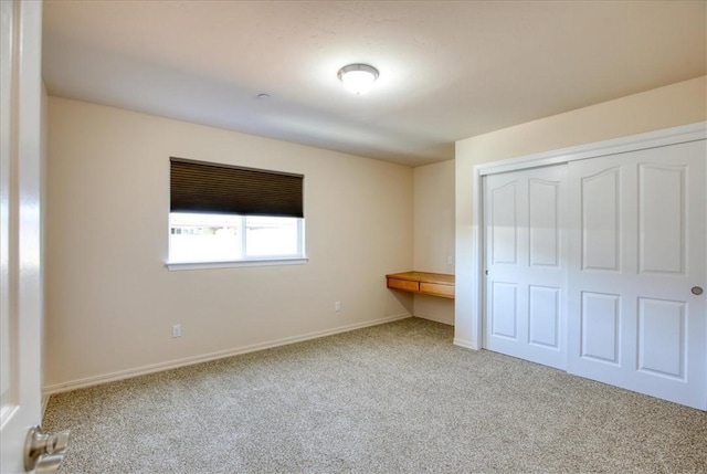 unfurnished bedroom with light carpet, built in desk, and a closet