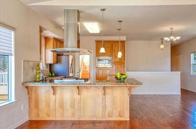 kitchen with island range hood, hanging light fixtures, appliances with stainless steel finishes, kitchen peninsula, and hardwood / wood-style floors