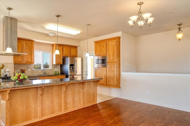 kitchen featuring appliances with stainless steel finishes, island exhaust hood, dark stone counters, hardwood / wood-style floors, and backsplash