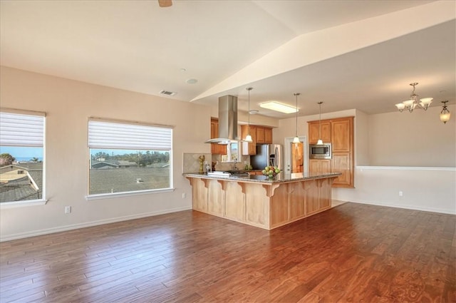 kitchen with pendant lighting, a breakfast bar area, appliances with stainless steel finishes, island exhaust hood, and kitchen peninsula