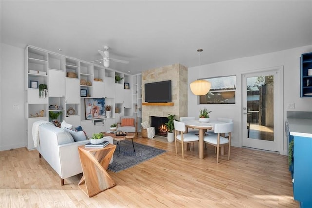 living room with ceiling fan, a stone fireplace, and light hardwood / wood-style floors