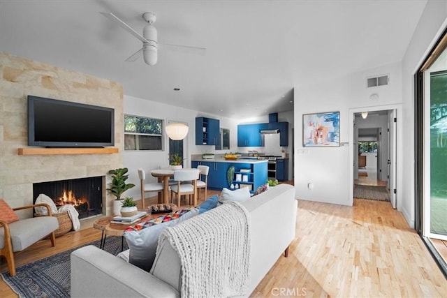 living room featuring ceiling fan, plenty of natural light, a large fireplace, and light wood-type flooring