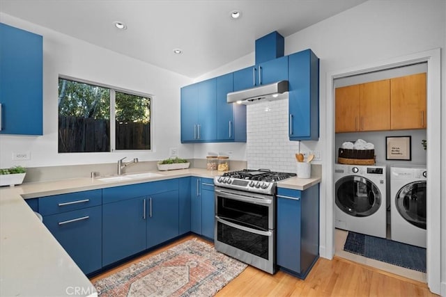 kitchen featuring washer and dryer, sink, double oven range, blue cabinetry, and light hardwood / wood-style flooring