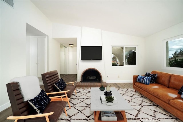 living room with lofted ceiling, hardwood / wood-style flooring, and a large fireplace