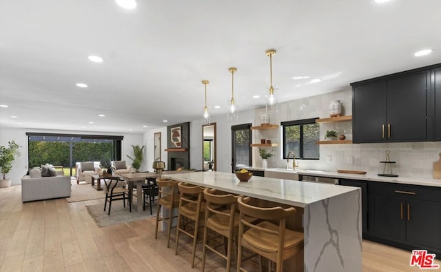 kitchen with a kitchen bar, hanging light fixtures, light wood-type flooring, a kitchen island, and light stone countertops