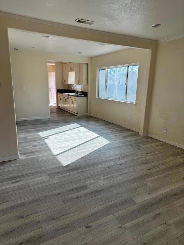 unfurnished living room with ornamental molding, a textured ceiling, and light wood-type flooring