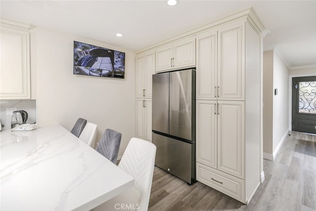 kitchen featuring a breakfast bar area, stainless steel fridge, ornamental molding, light stone countertops, and light wood-type flooring