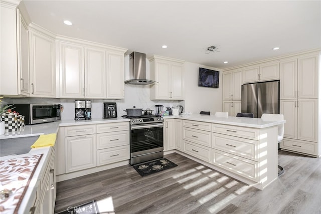 kitchen featuring stainless steel appliances, wall chimney range hood, light wood-type flooring, and kitchen peninsula