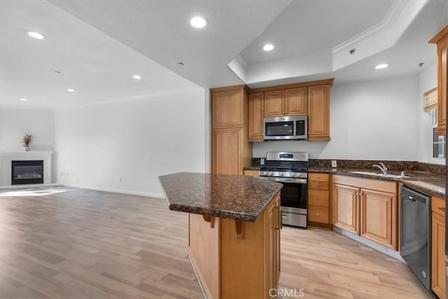 kitchen with a kitchen bar, appliances with stainless steel finishes, a raised ceiling, a kitchen island, and light hardwood / wood-style floors