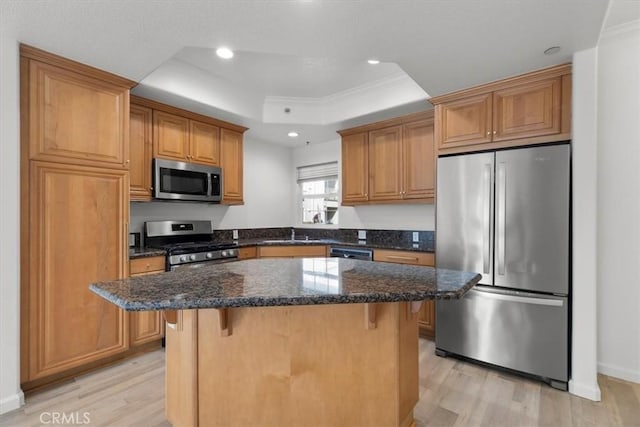 kitchen featuring a breakfast bar, appliances with stainless steel finishes, a tray ceiling, a kitchen island, and dark stone counters