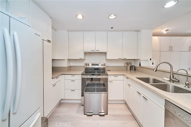 kitchen with stainless steel appliances, white cabinetry, sink, and light hardwood / wood-style floors