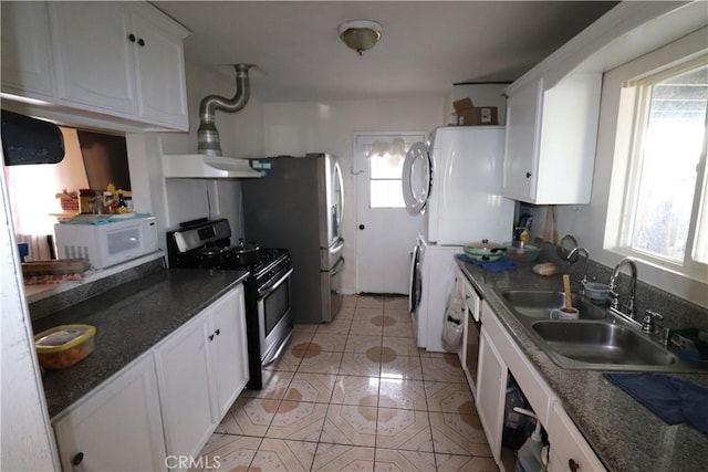 kitchen featuring sink, light tile patterned floors, stacked washer and clothes dryer, stainless steel range with gas stovetop, and white cabinets