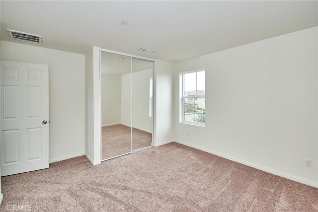 unfurnished bedroom with light colored carpet and a closet