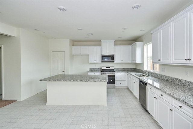 kitchen with a kitchen island, sink, white cabinets, light stone counters, and stainless steel appliances