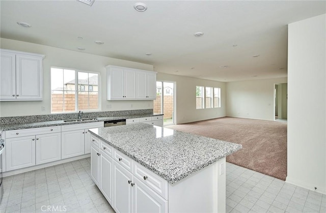 kitchen with sink, a center island, light stone counters, white cabinets, and light carpet