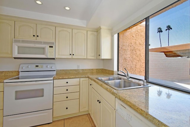 kitchen with sink, light tile patterned floors, light stone counters, white appliances, and cream cabinetry