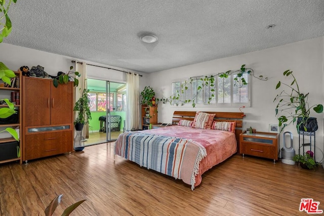 bedroom with hardwood / wood-style flooring, access to outside, and a textured ceiling