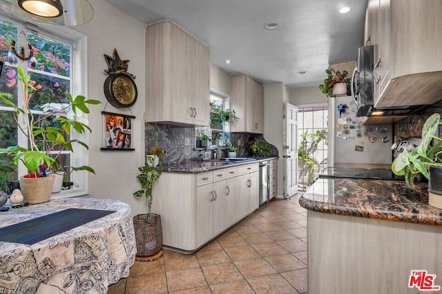 kitchen with sink, light tile patterned floors, backsplash, stainless steel appliances, and dark stone counters