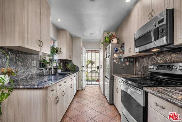 kitchen featuring light brown cabinetry, sink, dark stone countertops, light tile patterned floors, and stainless steel appliances