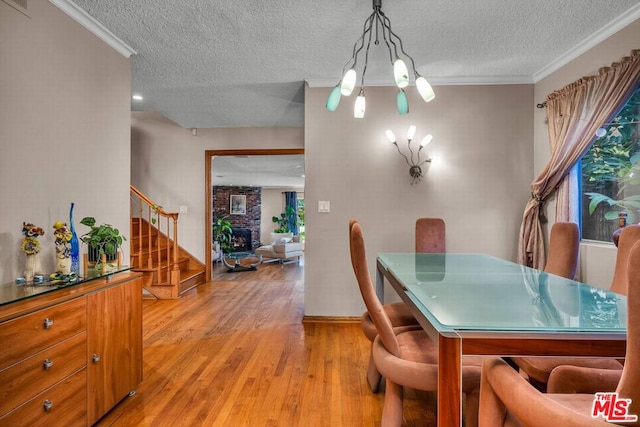 dining area featuring crown molding, a fireplace, light hardwood / wood-style flooring, and a textured ceiling