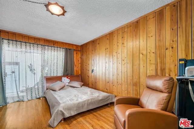 bedroom with a textured ceiling, light hardwood / wood-style flooring, and wood walls