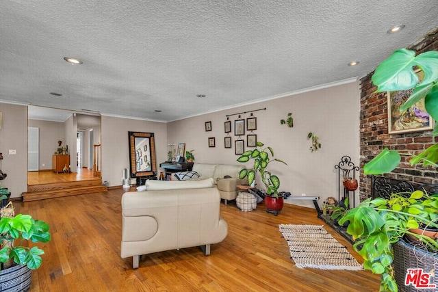 living room with a brick fireplace, light hardwood / wood-style flooring, ornamental molding, and a textured ceiling