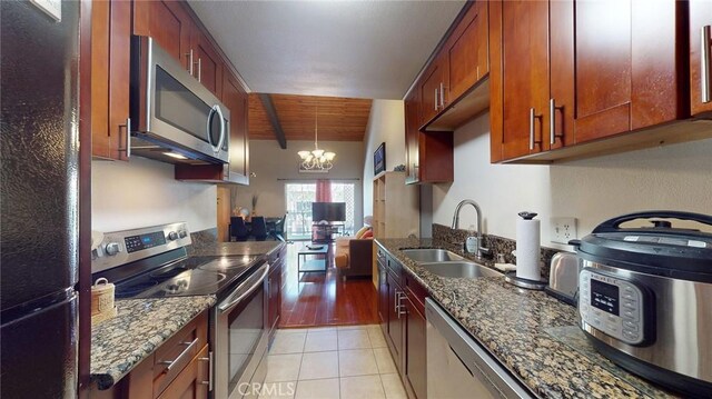 kitchen with light tile patterned flooring, sink, dark stone countertops, stainless steel appliances, and an inviting chandelier