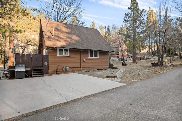 view of home's exterior with a shingled roof and a patio area