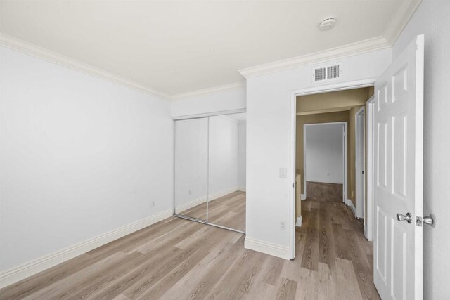 unfurnished bedroom with crown molding, a closet, visible vents, light wood-type flooring, and baseboards