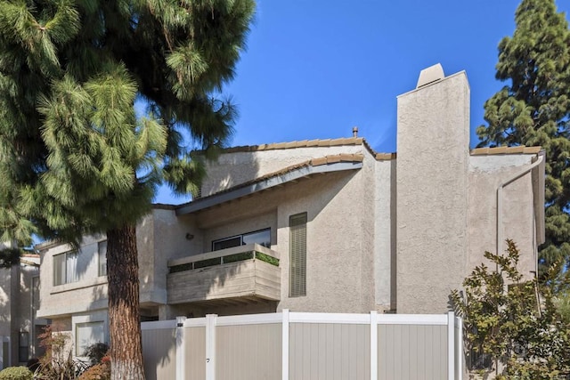 view of side of property featuring a chimney, fence, a balcony, and stucco siding