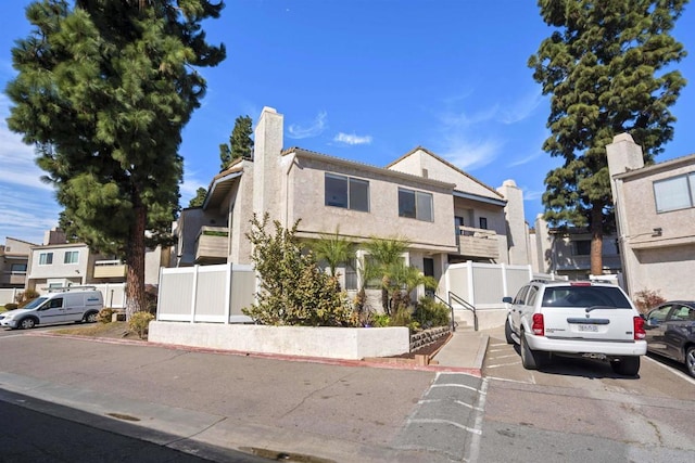 view of front facade with a chimney, fence, a residential view, and stucco siding