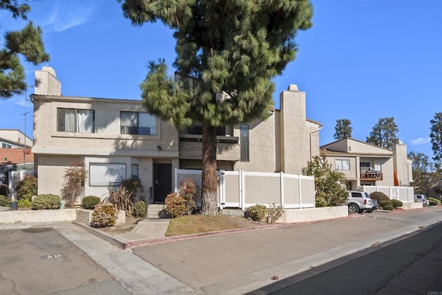 multi unit property with fence, a chimney, and stucco siding