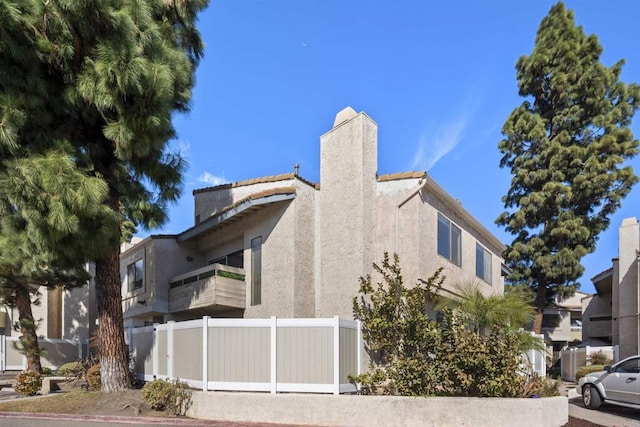 view of property exterior with a chimney, fence, and stucco siding