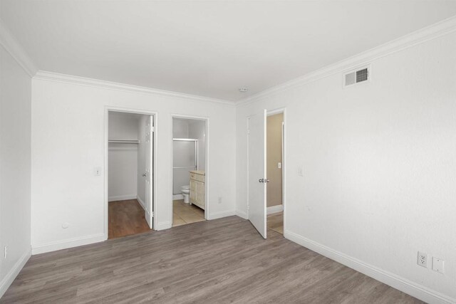 unfurnished bedroom featuring visible vents, baseboards, a closet, light wood-type flooring, and crown molding