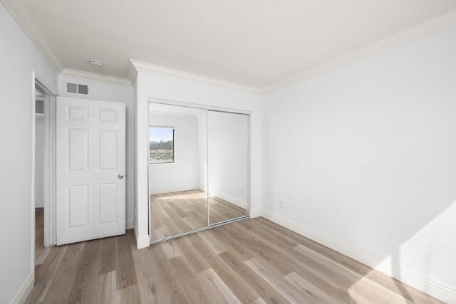 unfurnished bedroom featuring a closet, visible vents, ornamental molding, light wood-type flooring, and baseboards